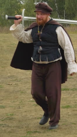 red-bearded squire with sword and teenage girl with ax walk across lawn talking cheerfully. medieval people prepare for combat training in nature horizon tilts