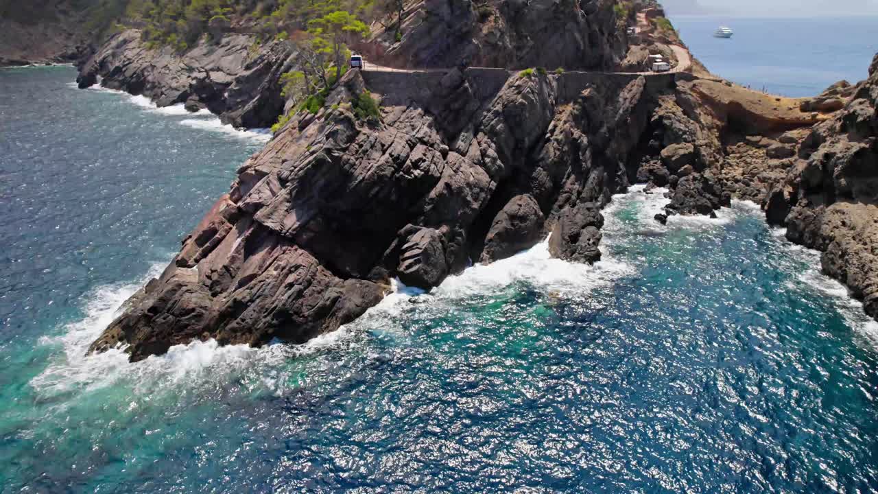 Caletta rocciosa con onde che si infrangono a cerchio, ripresa da drone.