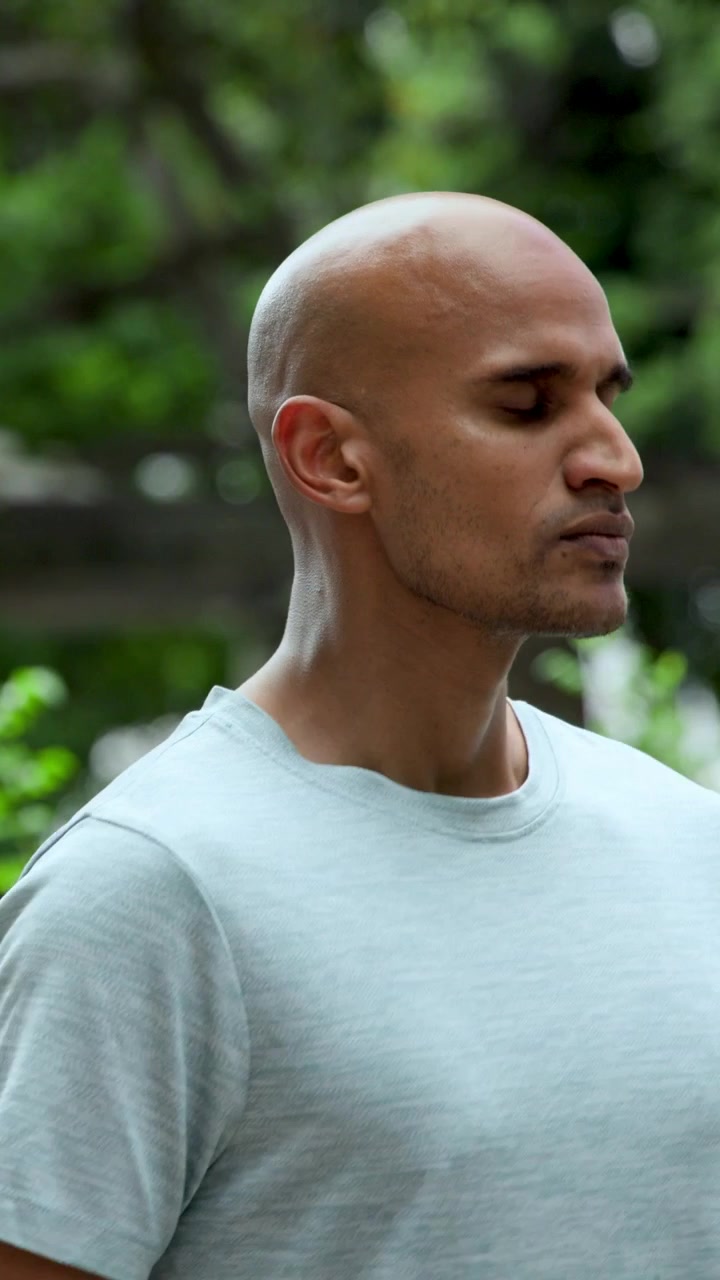 Vertical video: Inhaling, bald man in pale blue tee at park calling, turning and stepping right