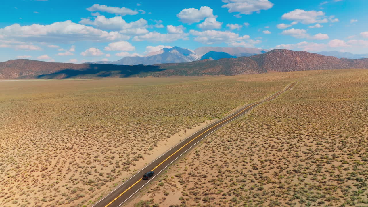 Two-lane road leading to the beautiful mountains. Highway to Nevada from California at backdrop of blue skies with fluffy clouds. Aerial view.