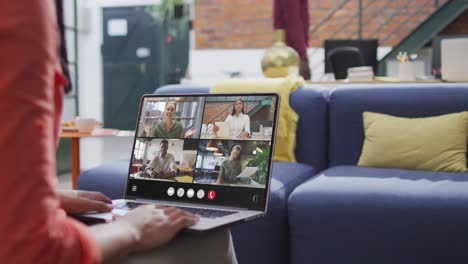 Biracial-woman-using-laptop-for-video-call,-with-diverse-business-colleagues-on-screen