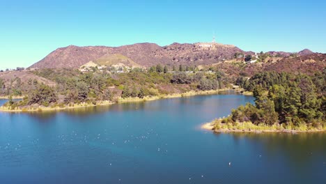 reverse aerial over the dam at the hollywood reservoir in the hollywood hills with hollywood sign distant