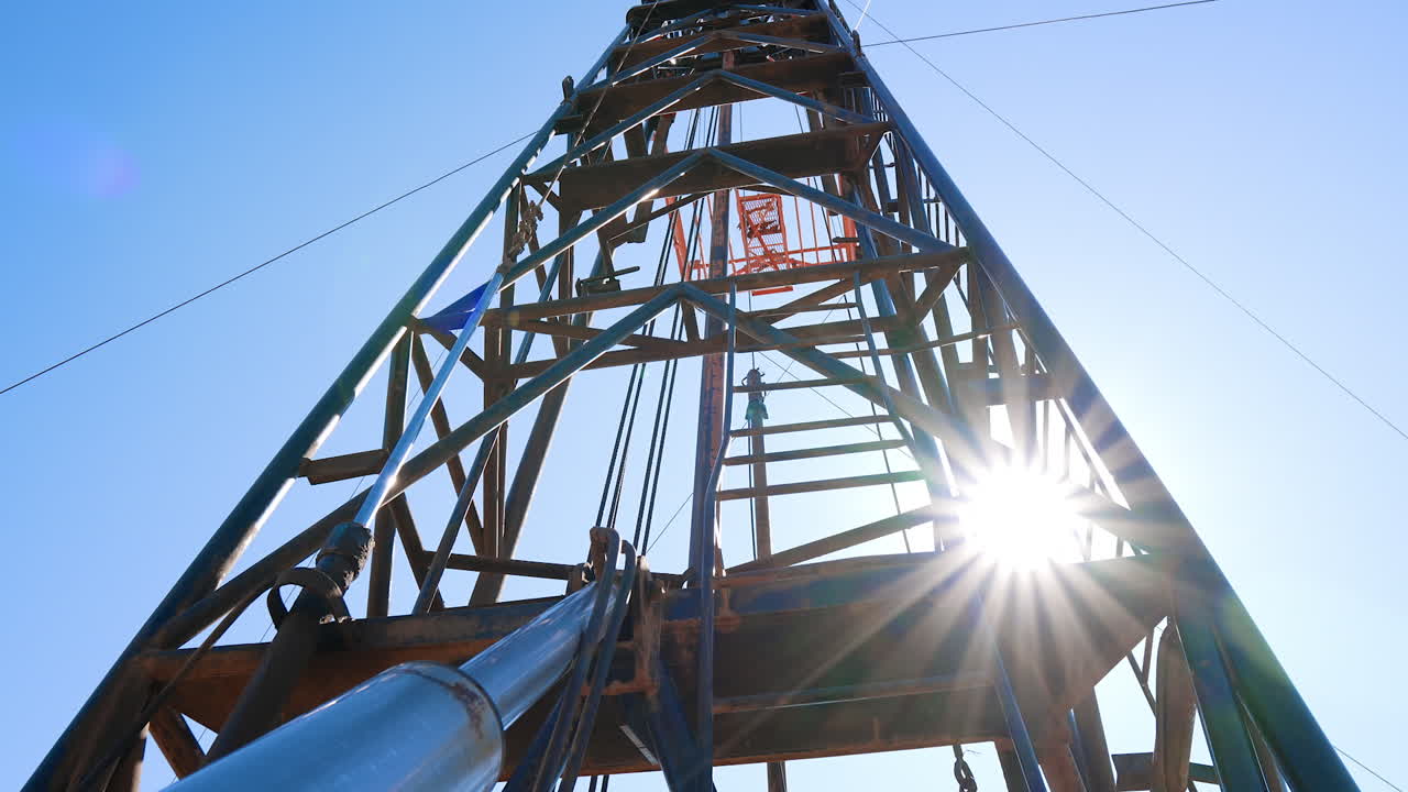 Metal construction tower with the equipment for drilling natural resources. Standing at the foot and looking up to a derrick at the site for oil production.