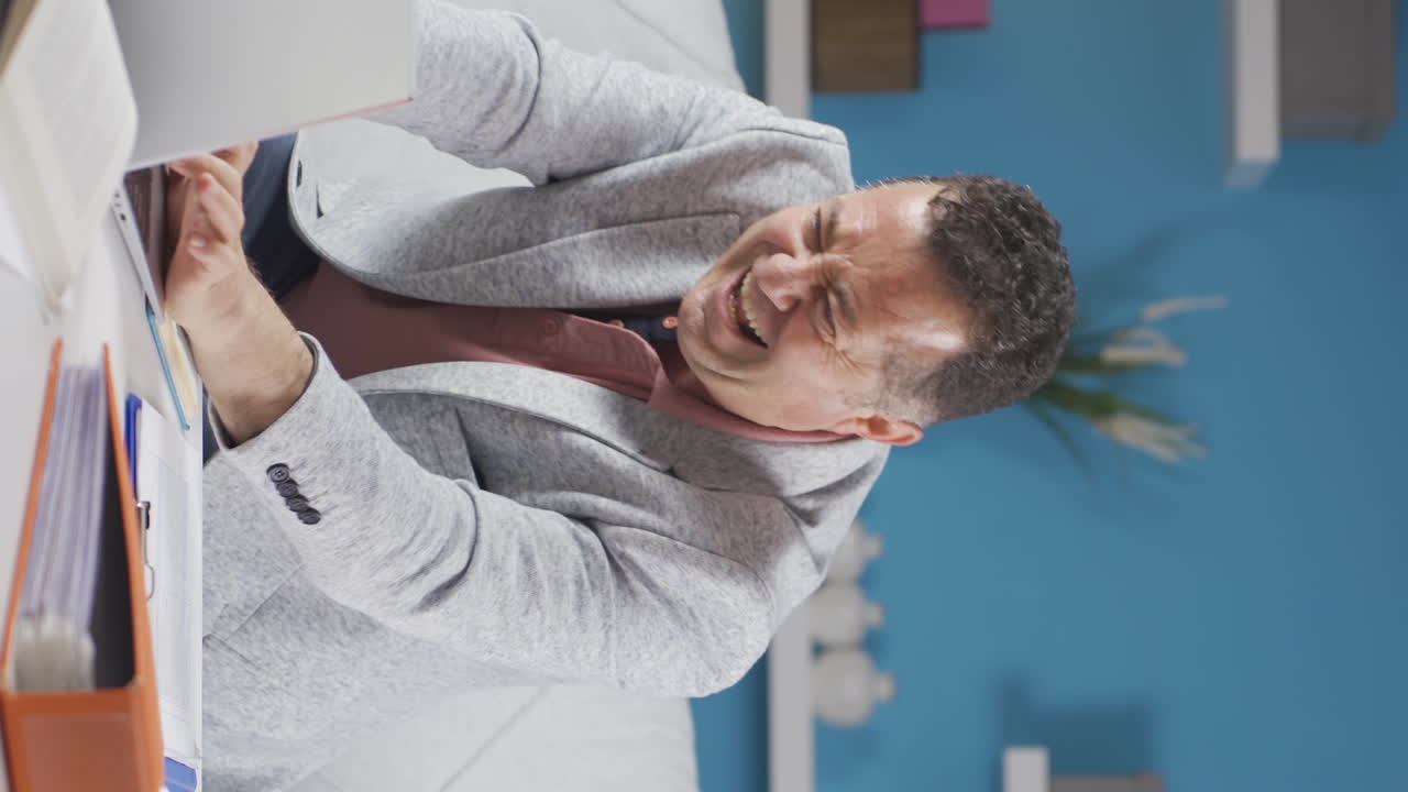 video vertical de un trabajador de oficina en casa, un anciano divertido trabajando en una computadora portátil, usándola.