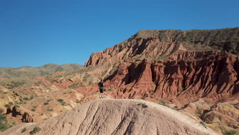 Man-standing-on-canyon-ridge-at-Fairy-Tale-Canyon-near-Issyk-Kul-Lake-in-Karakol,-Kyrgyzstan,-aerial-drone-shot