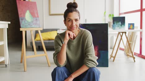 video de una feliz artista femenina biracial en el estudio mirando a la cámara