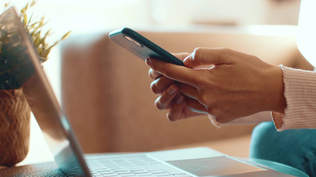 Person Using Smartphone While Working on Laptop
