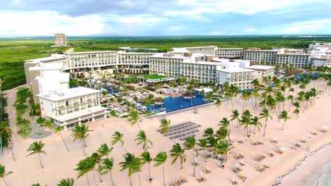 Luxury-vacation-resort-with-swimming-pools,-sand-beach-with-palm-trees-and-clear-turquoise-sea-in-Dominican-Republic,-aerial-view-of-tropical-tourist-hotel-in-Punta-Cana