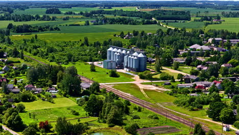 a drone captures a modern grain elevator complex in the latvian countryside, strategically located by a railway for efficient agricultural logistics, transport, and export of the harvest