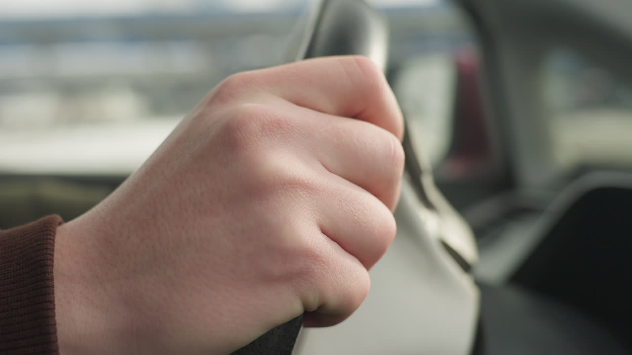 close up of driver resting hand on steering wheel while gently tapping surface, focus on hand position with soft natural light and blurred winter background outside side window
