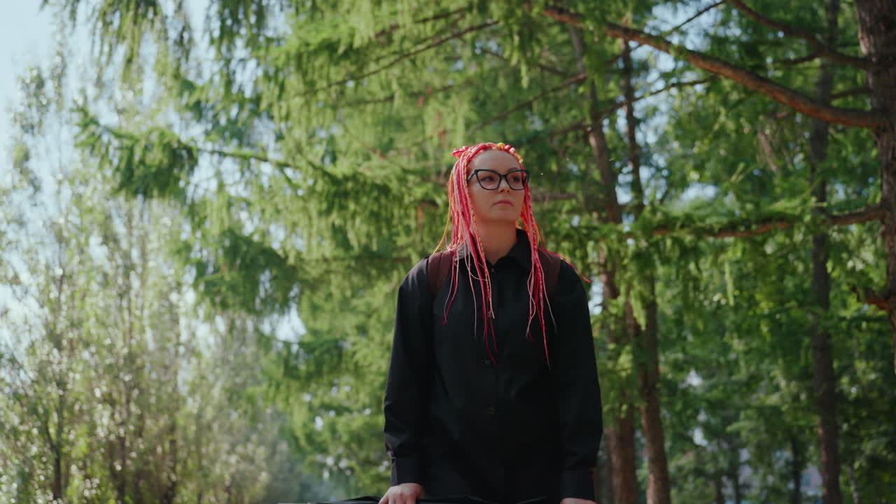 자전거를 든 여성, 평화로운 햇살이 비치는 야외에서 자전거를 들고 있는 백인 여성, 조용한 공원에서 안경을 쓰고 강렬한 빨간색 드레드락을 한 채 자전거 옆에 서서 생각에 잠긴 여성