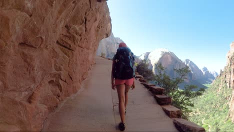 Young-woman-wearing-backpack-is-walking-to-Angel's-Landing-in-Zion-National-park-in-Utah,-USA