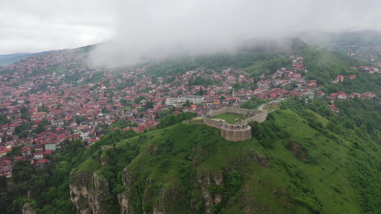 Bosna-Hersek'in Saraybosna şehrinin sisli çevresinde yemyeşil dağların, kıvrımlı vadi yollarının ve yamaç evlerinin üzerinde yayılan alçak bulutların ve sisin dramatik havadan drone görüntüsü