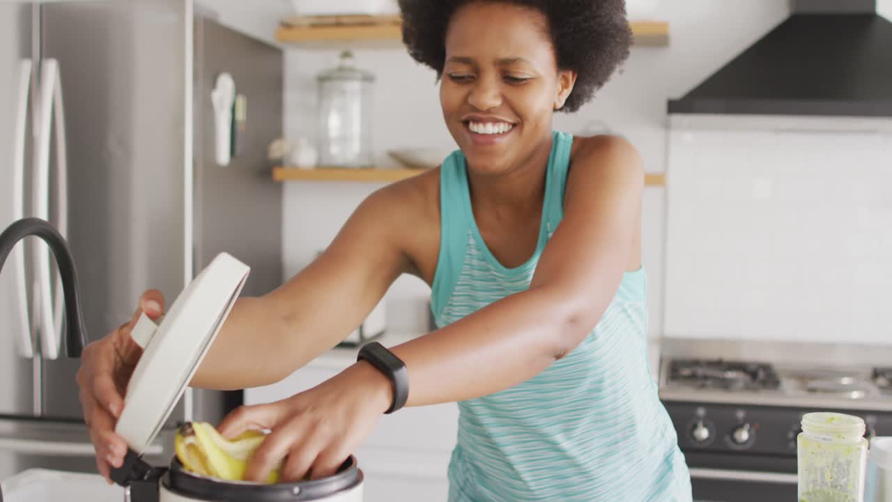 Donna afroamericana felice che pulisce, gettando i rifiuti in cucina
