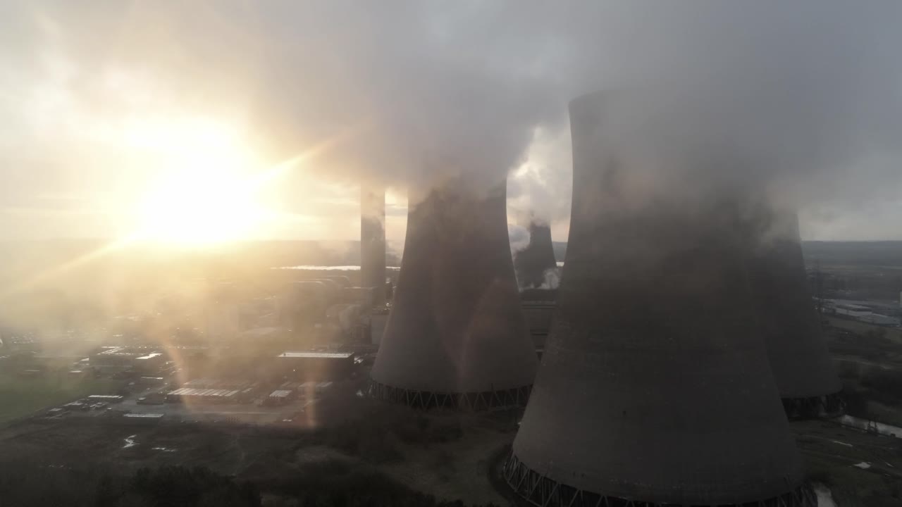 Vista aerea con lento movimento dolly verso sinistra delle torri di raffreddamento di una centrale elettrica del Regno Unito, emissioni di fumo e vapore all'alba