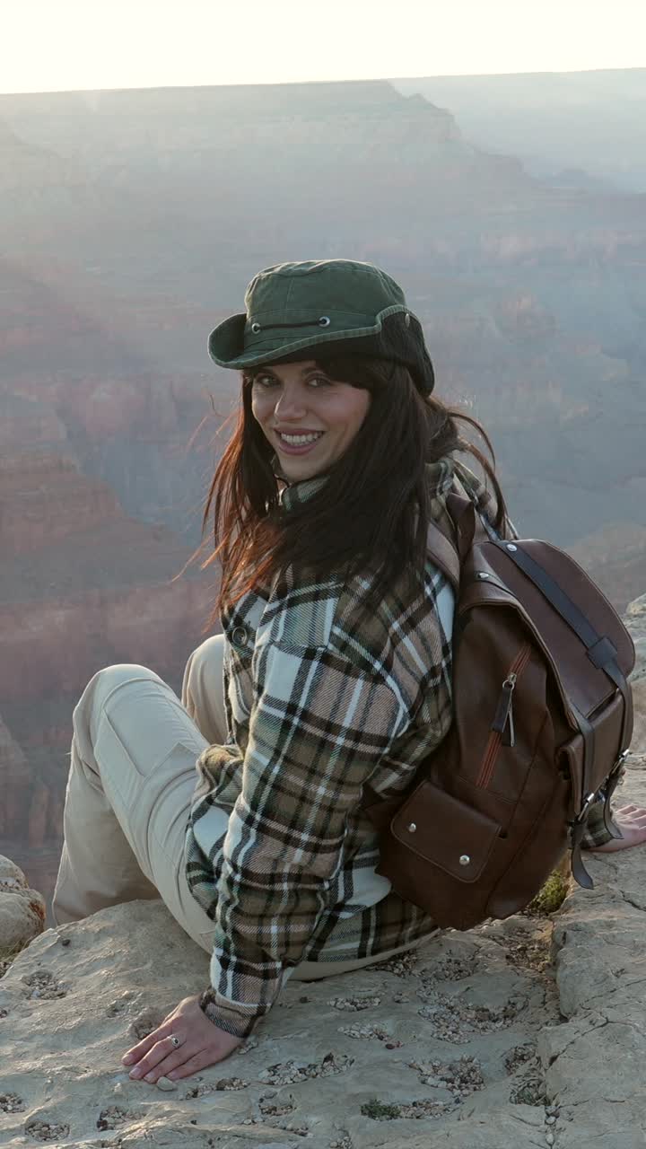 Donna sorridente con zaino seduta sul bordo del Grand Canyon