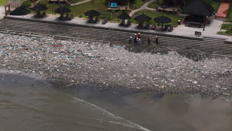 aerial backwards from people cleaning up trash on beach revealing ham tien village