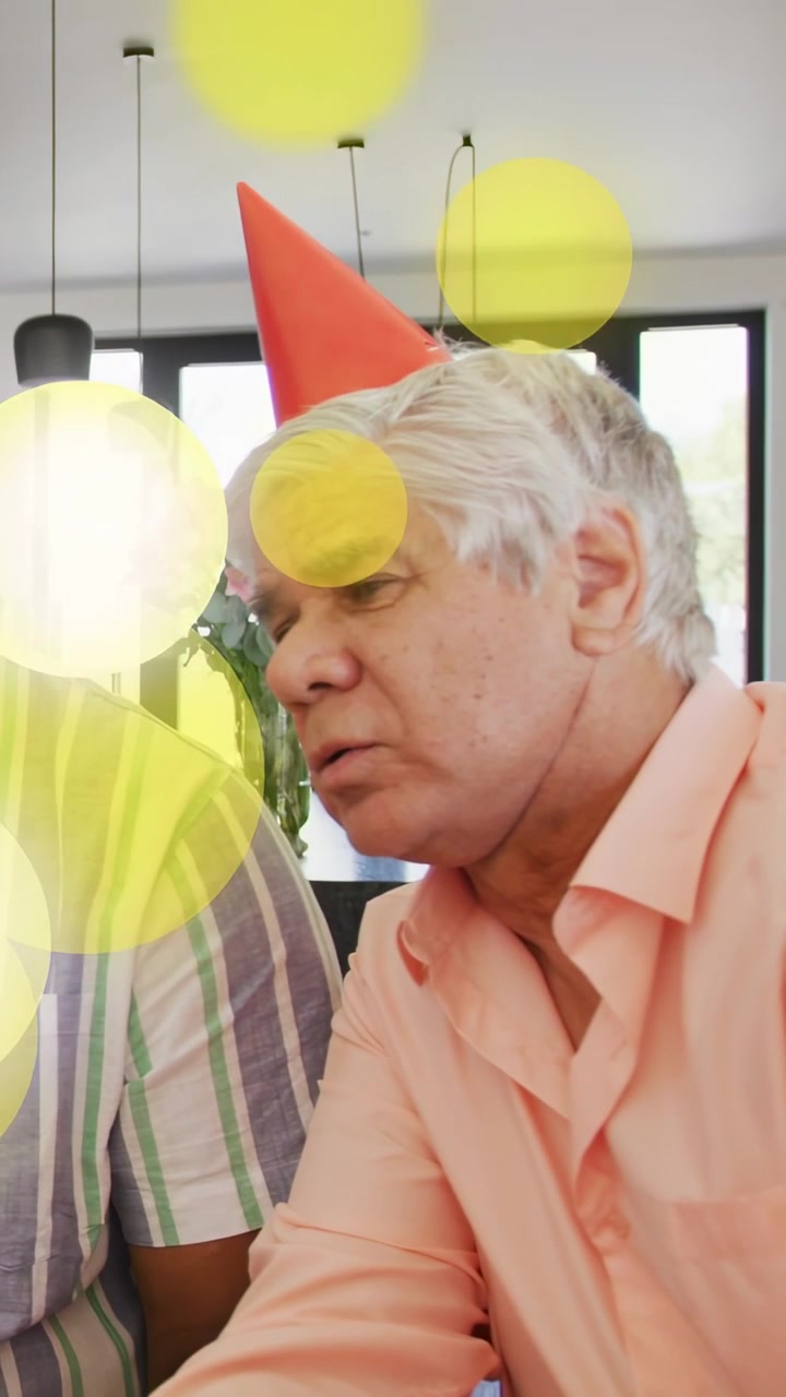 Vertical video: Senior man wearing hat leaning and talking, yellow bokeh sweeping face during party