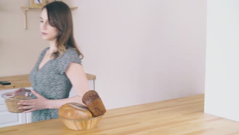 lady carries bowl of grains puts by bread in modern kitchen