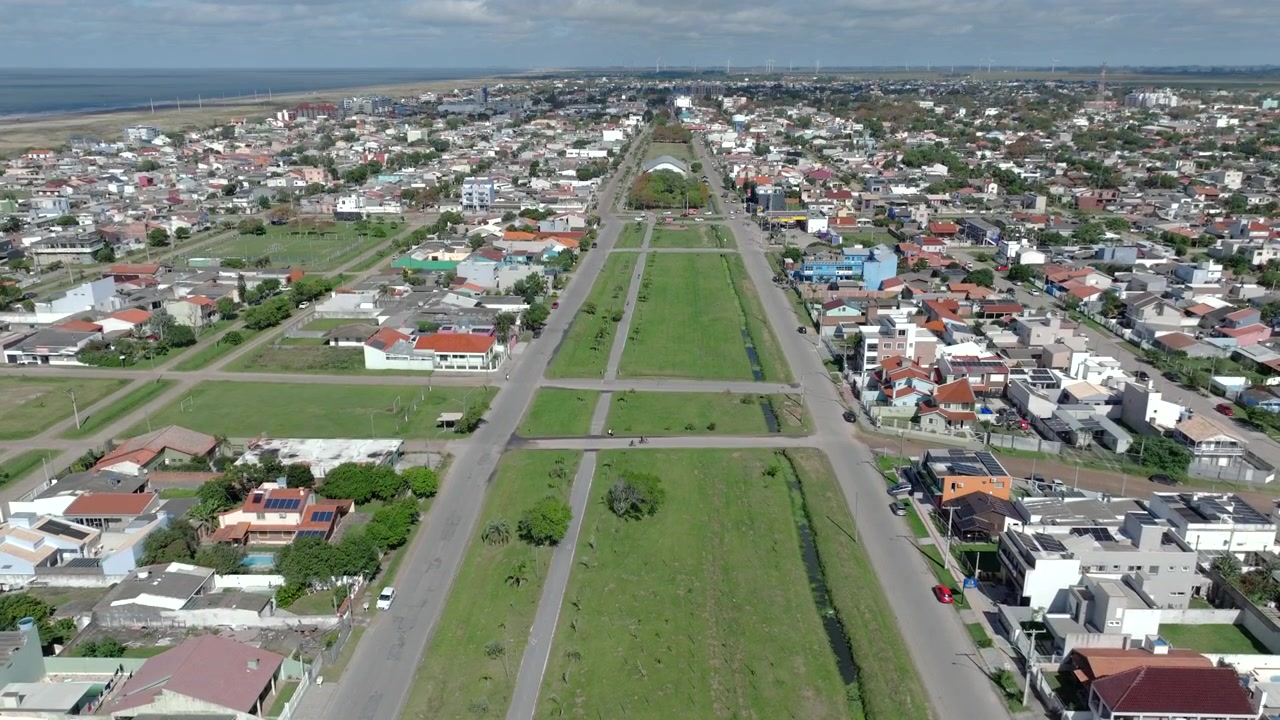 Ripresa aerea con drone sulla città balneare di Balneario Cassino con un ampio viale alberato centrale verde e un canale di scolo, Rio Grande do Sul, Brasile