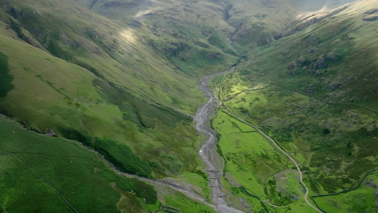 Stream Winding Through Deep Sided Green Valley With Pools Of Summer Sunshine Moving Over Landscape. Crinkle Crags, Great Langdale, Lake District, Cumbria, UK