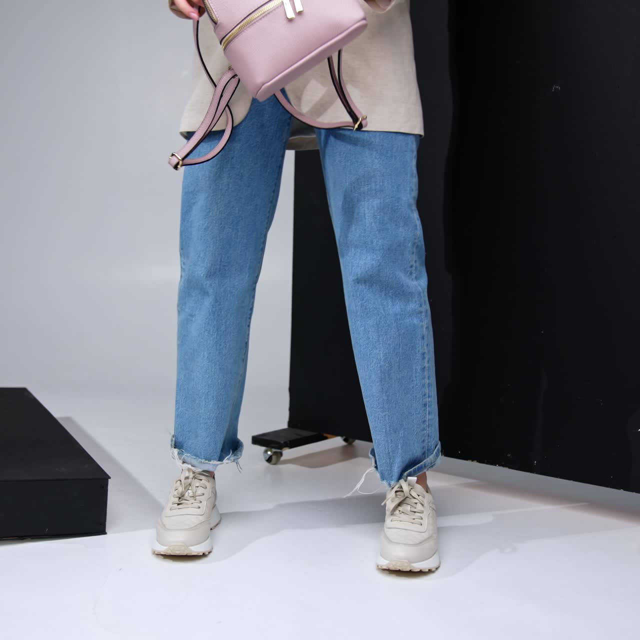 Unrecognized female wearing jeans and jacket holding a bag. Model in sports shoes standing near the black screen