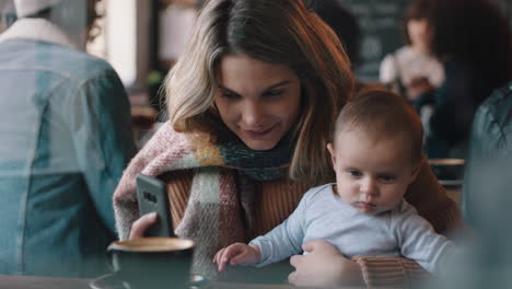 young mother with baby in cafe using smartphone drinking coffee relaxing in busy restaurant enjoying motherhood