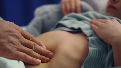 doctor hands touching stomach closeup. sick little girl lying in hospital bed.