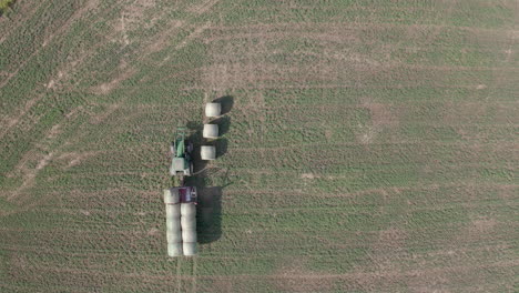 Ver-Directamente-Encima-De-La-Máquina-De-Tractor-Industrial-Verde-Cargando,-Recolectando,-Recolectando-Y-Transportando-Balas-De-Heno-En-Llanuras-Rurales-Y-Campos,-Saskatchewan,-Canadá,-Drones-Aéreos-Estáticos