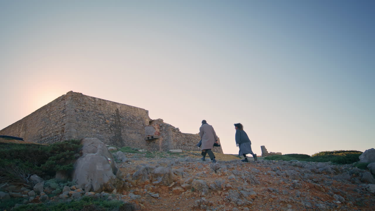 Coppia spensierata che corre su una collina al tramonto, con un castello abbandonato sullo sfondo. Coppia che cammina.