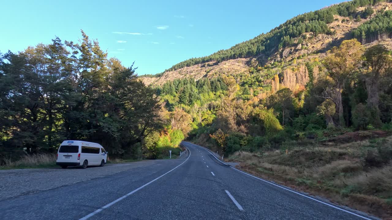 Vehicle travels winding mountain road, lush forest, daylight, smooth camera movement, clear blue sky