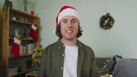 happy caucasian man in santa hat on christmas video call holding present and talking