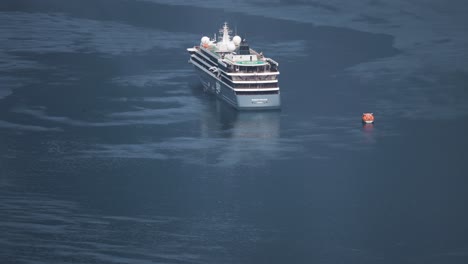 a large cruise ship is anchored in the calm waters of geiranger fjord, its reflection shimmering on the water's surface. motorboats cruise nearby.