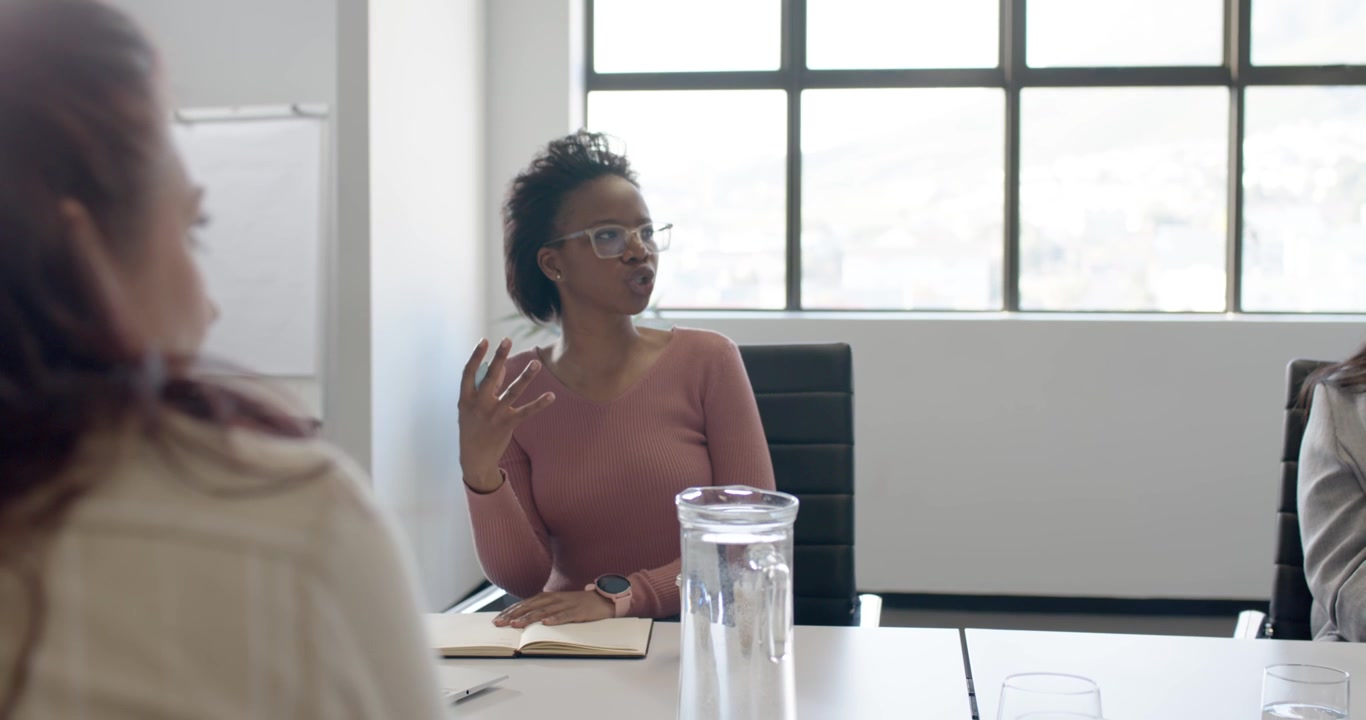 Shot panning to adult African American woman raising pen over notebook, leading meeting at table