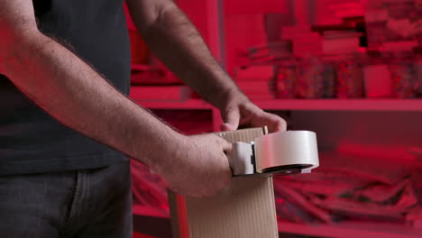 man packing product, sealing cardboard box with packaging tape