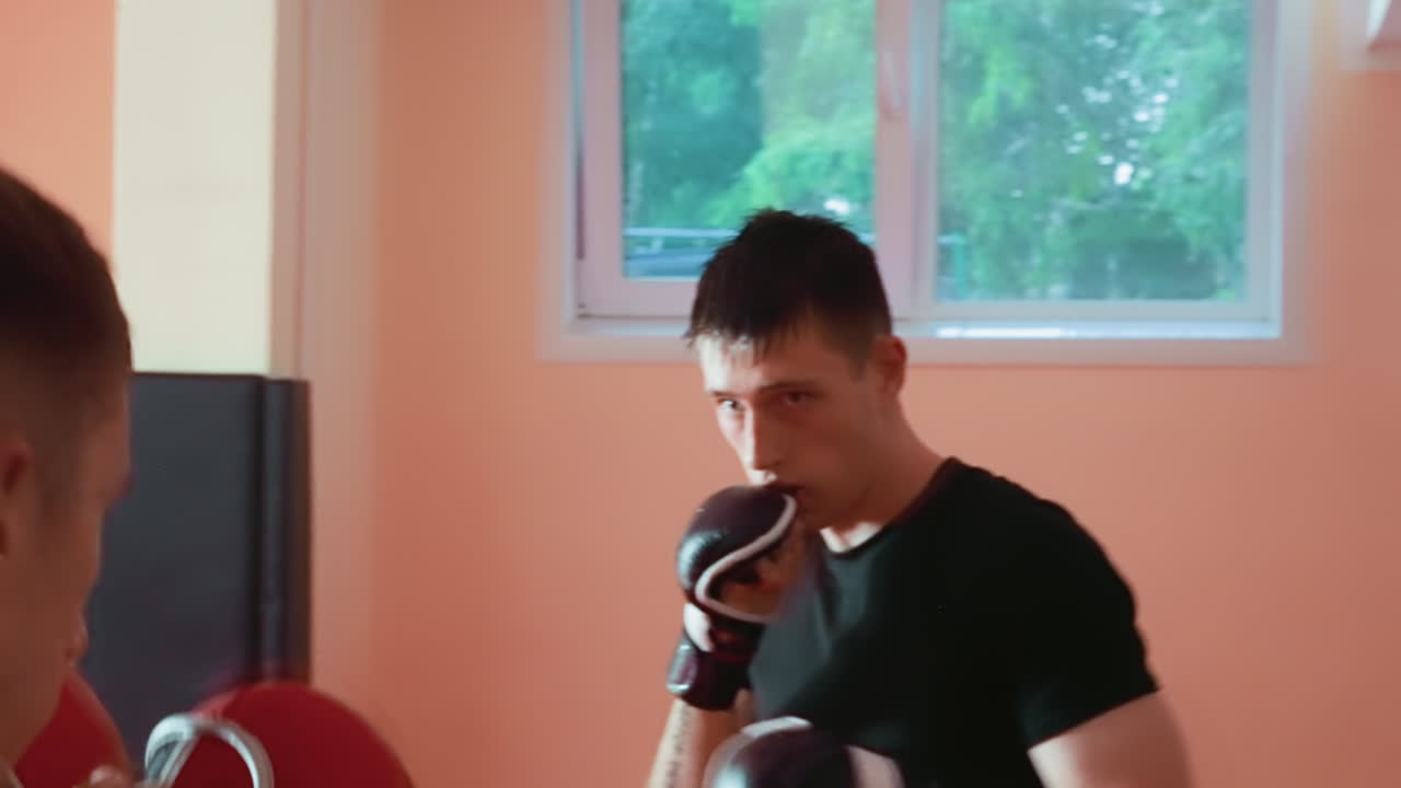 Pugilist in black shirt wearing gloves grapples opponent during combat training inside gym, showing intensity, control, discipline, focus, and power while engaged in sparring session with competitive energy