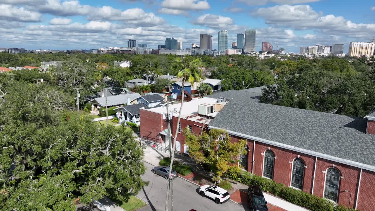 Quartiere di Hyde Park a Tampa, in Florida. Strade lussureggianti e alberate, edifici residenziali e palme. Skyline del centro di Tampa in lontananza. Ampia ripresa aerea frontale. Pedone che cammina sul marciapiede