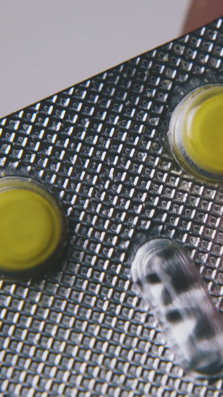 sick man holds silver blister with bright yellow pills by hands examining on light background extreme close view