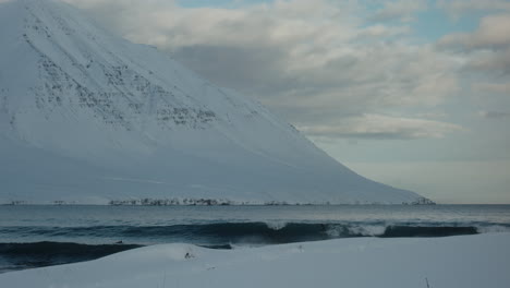 slow motion tracking follows surfer catching wave and riding down face at base of snowy mountain