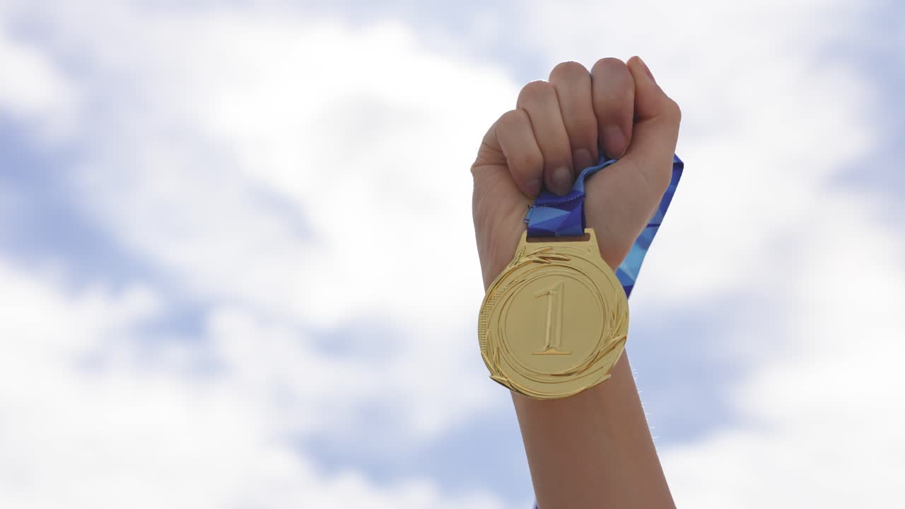 Hand lifting a winning medal against the sky background. Concept of success, achievement, motivation, and recognition. Symbol of victory, reward, and accomplishment