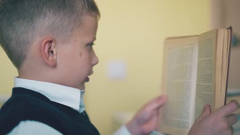 Un-Lindo-Colegial-Lee-Un-Libro-De-Texto-Pasando-La-Página-En-La-Mesa-De-La-Habitación