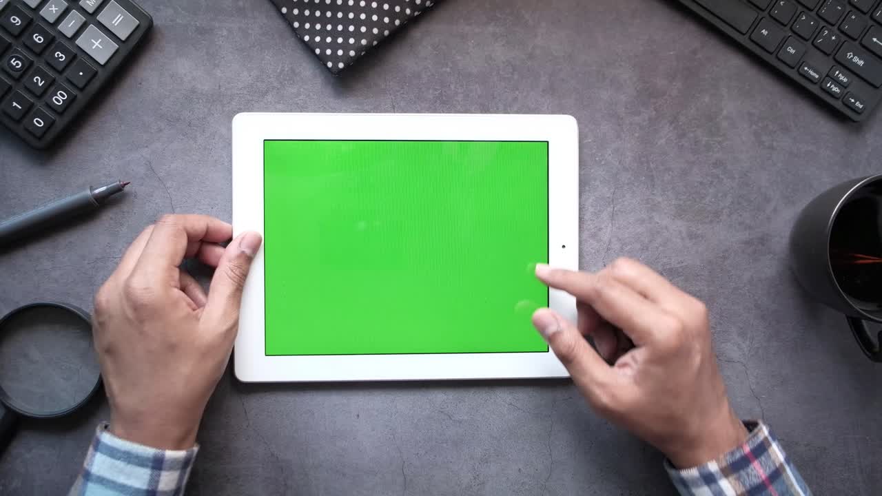 책상 위에 초록색 화면을 가진 태블릿을 사용하는 사람