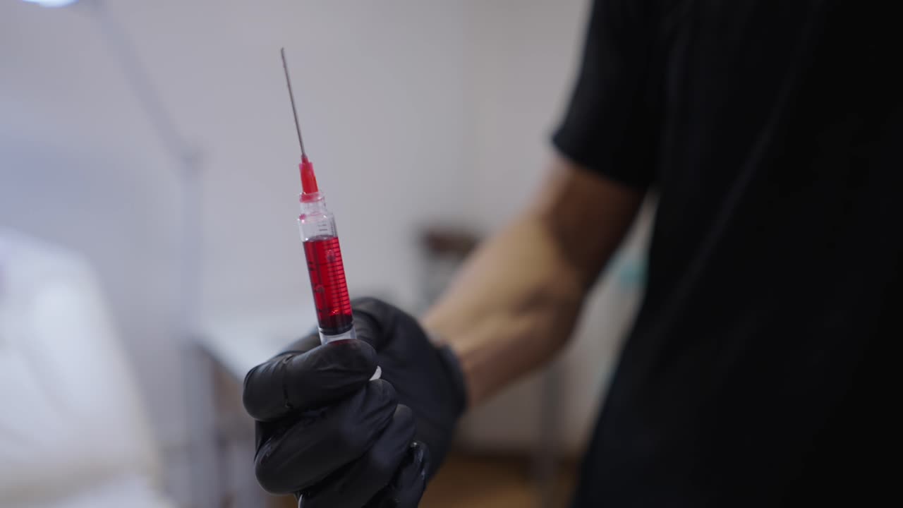 Close-up of a gloved hand holding a syringe with red liquid