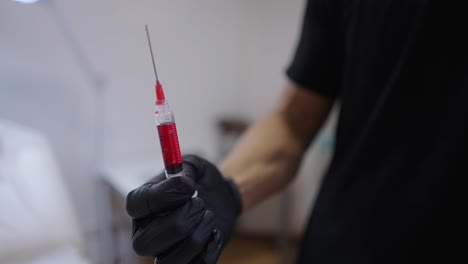 close-up of a gloved hand holding a syringe with red liquid