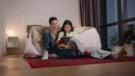 couple watching interesting movie on tablet while sitting on the floor at home