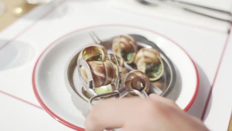 hands struggling to grab escargots in they shells with utensils