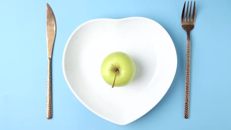 una sola manzana verde en un plato en forma de corazón con cubiertos