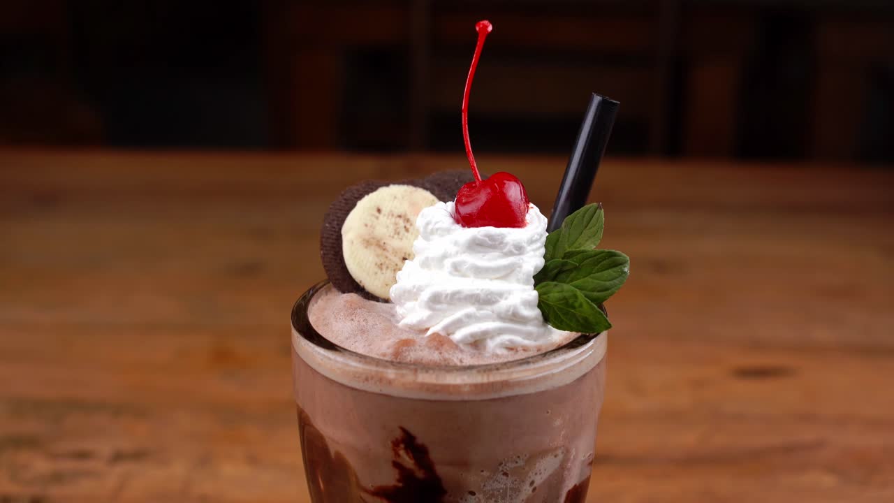 Detailed close up of chocolate milkshake, with caramel, espresso coffee and whipped cream with cherry, hand taking the cherry from the whipped cream