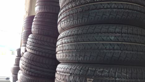 tall stacks of rubber car tires arranged indoors at a tire shop. natural daylight enters from the side. close-up descending motion.