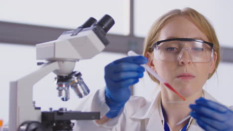 female lab worker putting blood sample onto slide for analysis under microscope